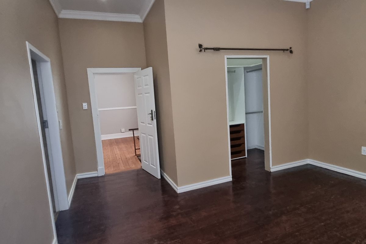 An empty bedroom featuring dark wooden flooring, neutral wall tones, and a built-in wardrobe with internal shelving.