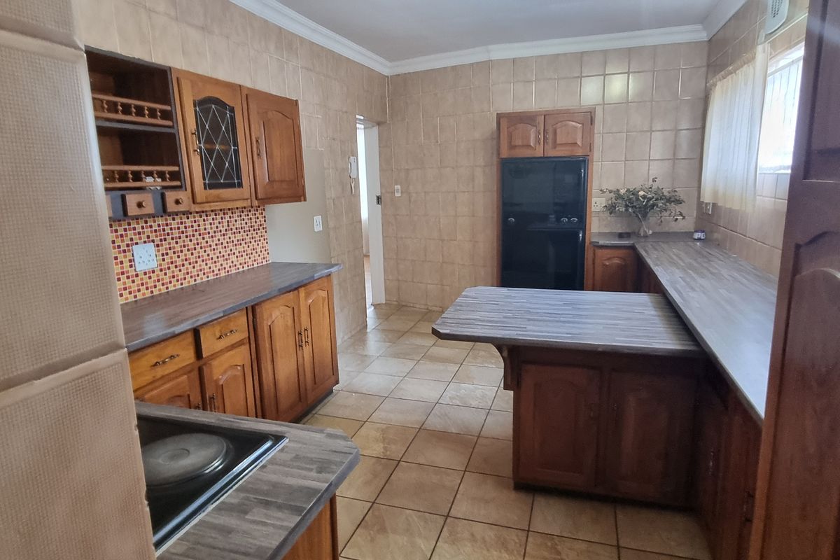 A functional kitchen featuring traditional wooden cabinetry, tiled wall finishes, and a built-in hob and oven setup with ample counter space.