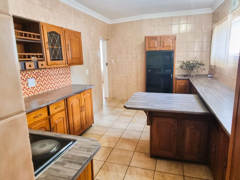 A functional kitchen featuring traditional wooden cabinetry, laminate countertops, and full-height ceramic wall tiling, offering a classic layout with ample storage space.
