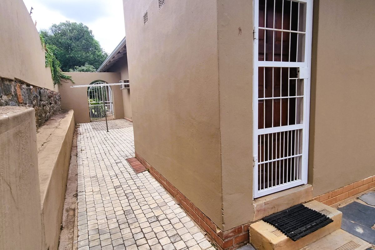 A side exterior view showing a paved walkway, stone retaining wall, and a secure entrance door with metal security bars.