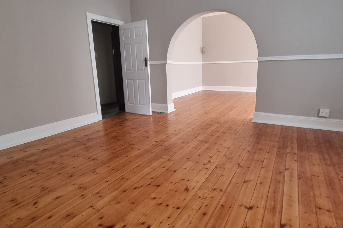 Spacious living area featuring polished timber flooring, a classic architectural archway, and neutral wall tones with decorative chair rail molding.
