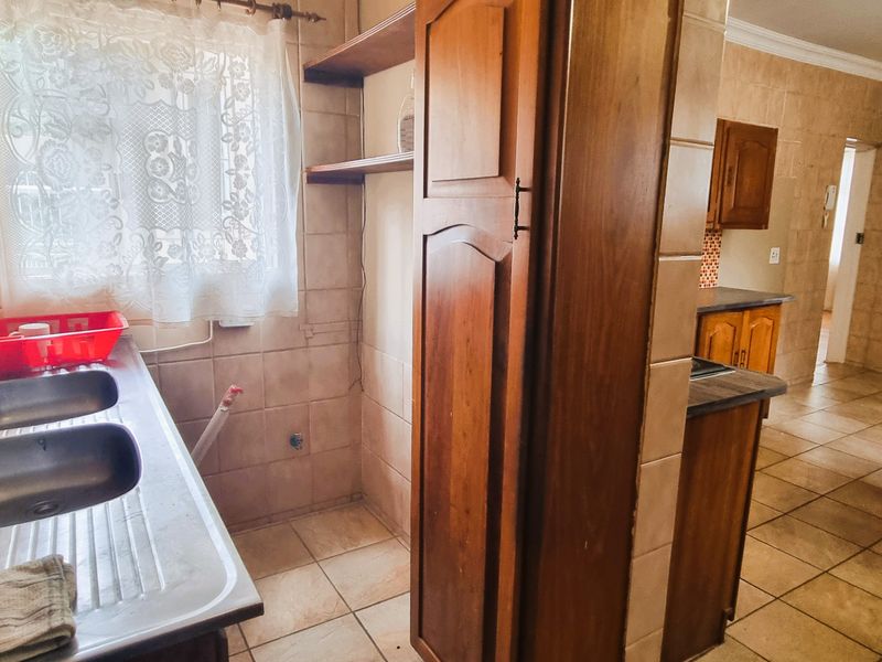 A functional kitchen featuring tiled walls and flooring, built-in wooden cabinetry, and a double stainless steel sink with a tiled splashback.