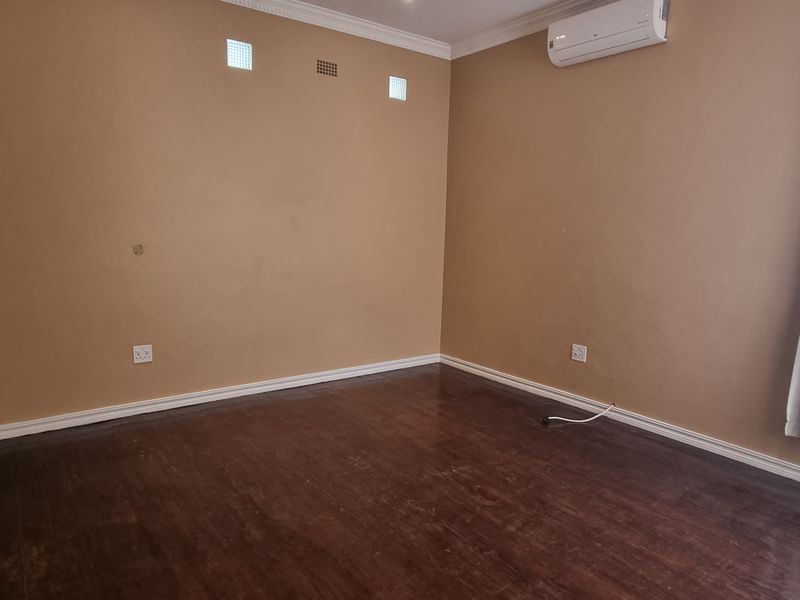 A spacious, empty bedroom featuring dark laminate flooring, neutral wall tones, and a wall-mounted air conditioning unit.