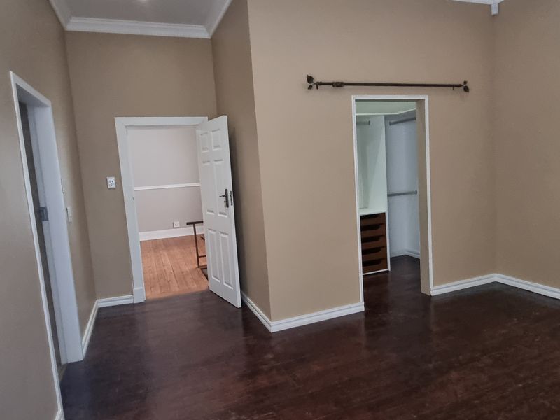 An empty bedroom featuring dark wooden flooring, neutral wall tones, and a built-in wardrobe with internal shelving.