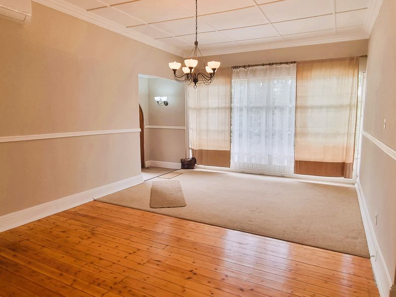 Spacious living area featuring polished hardwood floors, decorative ceiling tiles, and a classic archway, offering a bright and versatile space for relaxation.