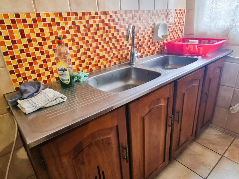A functional scullery area featuring a stainless steel double sink, wooden cabinetry, and a vibrant mosaic tile splashback.