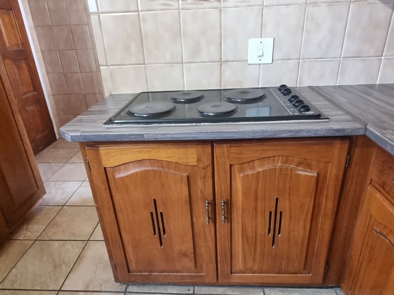 A functional kitchen area featuring wooden cabinetry, a built-in electric hob, and tiled splashbacks with a neutral countertop surface.