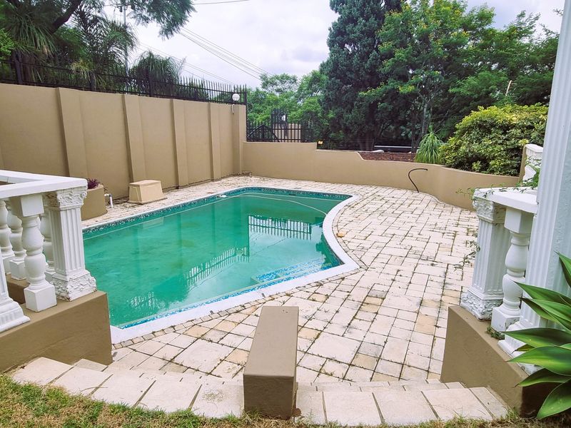 Outdoor pool area featuring a paved deck, perimeter boundary walls, and decorative classical columns, offering a private space for relaxation and entertainment.