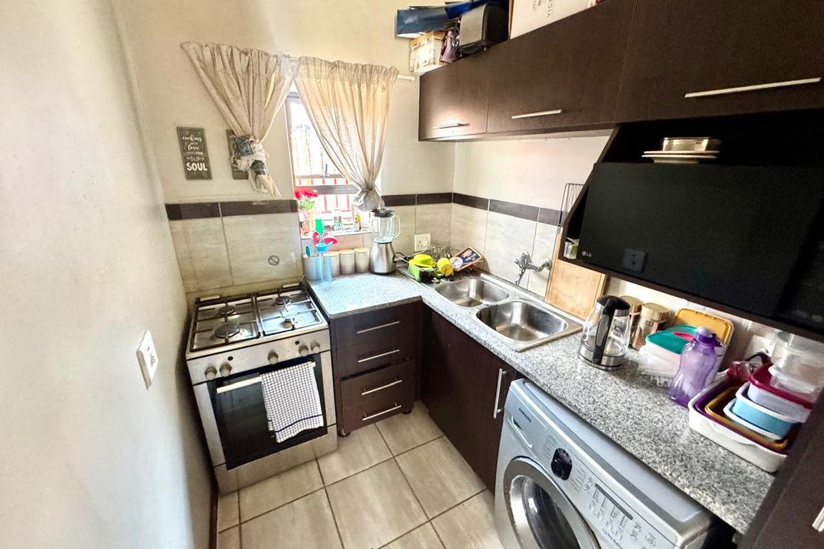 Compact kitchen featuring dark cabinetry, granite-look countertops, tiled flooring, a built-in stove with extractor fan, and a double stainless steel sink.