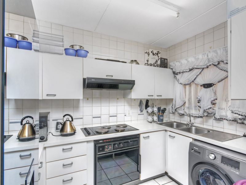 A functional kitchen featuring white cabinetry, an integrated electric hob and oven, extractor fan, and a double sink with tiled backsplash and flooring.