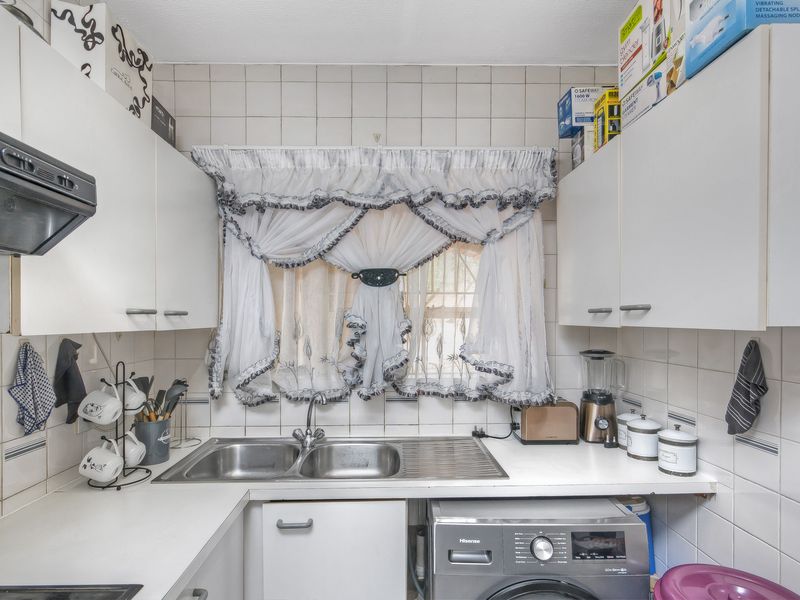 A functional kitchen featuring white cabinetry, a double bowl stainless steel sink, tiled splashbacks, and an integrated extractor fan.