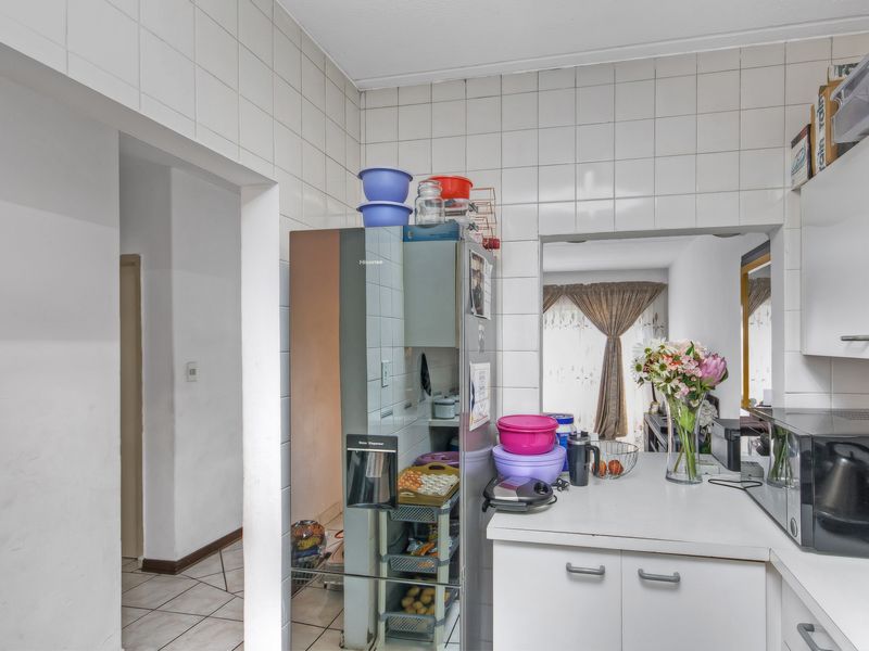 A compact kitchen featuring white tiled walls, built-in cabinetry, and laminate countertops, offering a functional layout with potential for modern updates.