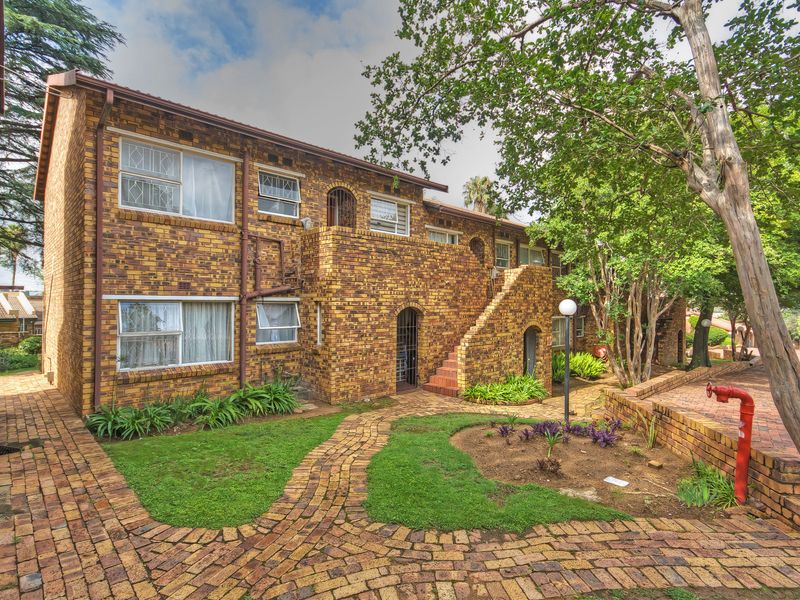 A view of the apartment complex exterior featuring face brick construction, paved walkways, landscaped garden areas, and an external staircase.