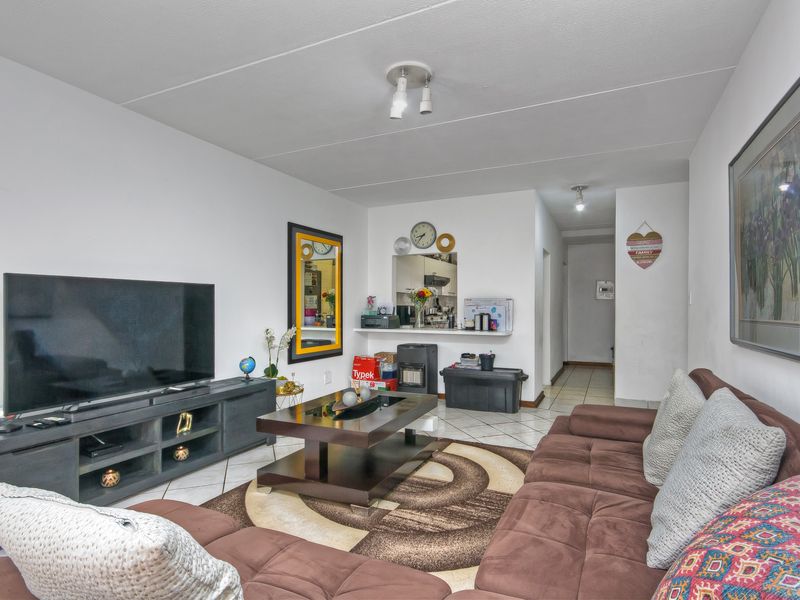 A living room featuring tiled flooring and a pass-through window connecting to the kitchen area, providing an open feel to the space.