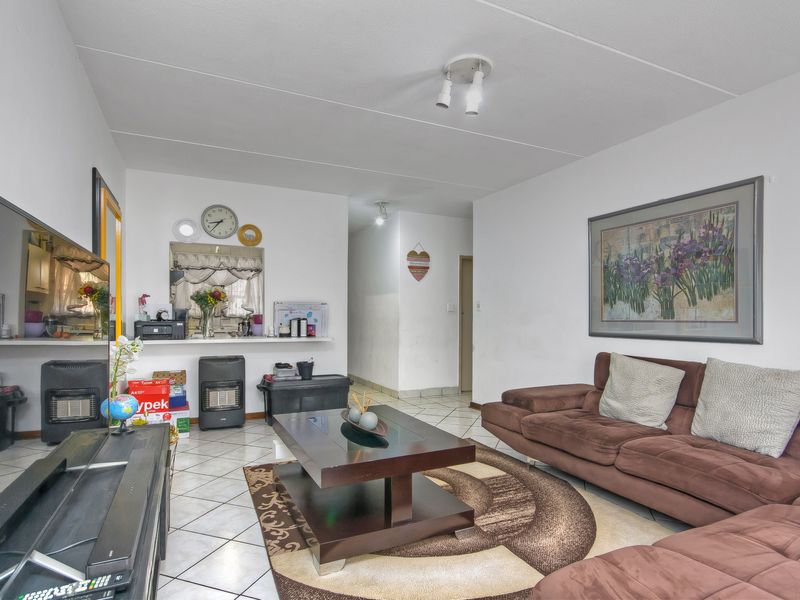 A living room featuring tiled flooring and a pass-through window connecting to the kitchen area, providing an open feel to the apartment layout.