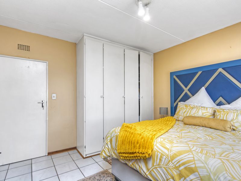 A bedroom featuring built-in wardrobes, tiled flooring, and a ceiling light fixture, offering a functional space with potential for cosmetic updates.