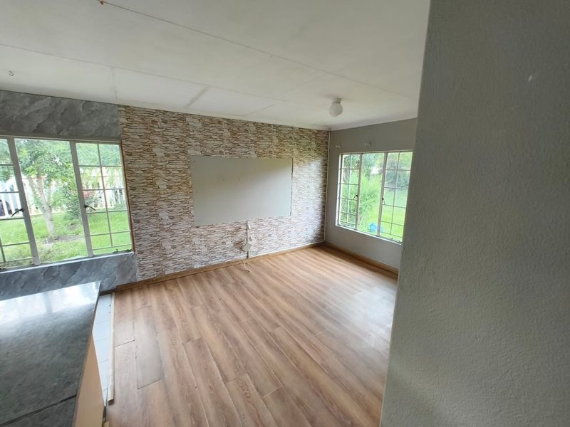 An empty living area featuring laminate flooring, large windows, and a textured feature wall with an unfinished central panel.
