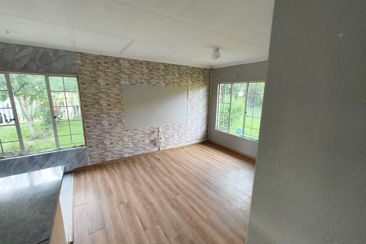 An empty living area featuring laminate flooring, large windows, and a textured feature wall with an unfinished central panel.