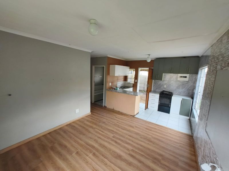 Open-plan living and kitchen area featuring laminate flooring, tiled kitchen workspace, and built-in cabinetry with a freestanding stove.