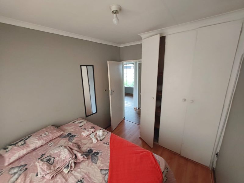 A functional bedroom featuring laminate flooring, built-in cupboards, and neutral wall finishes, providing a practical space with direct access to the hallway.
