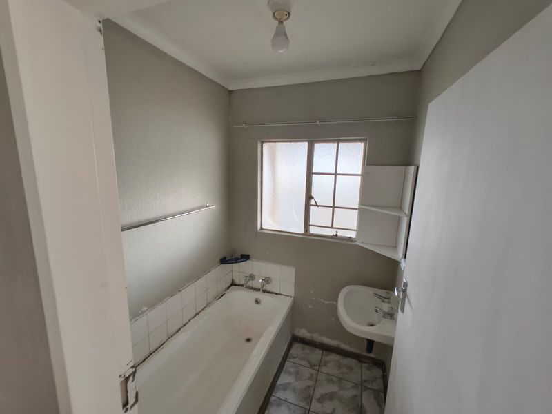 A compact bathroom featuring a bathtub, wall-mounted basin, and tiled flooring, currently in need of cosmetic updates and wall repairs.