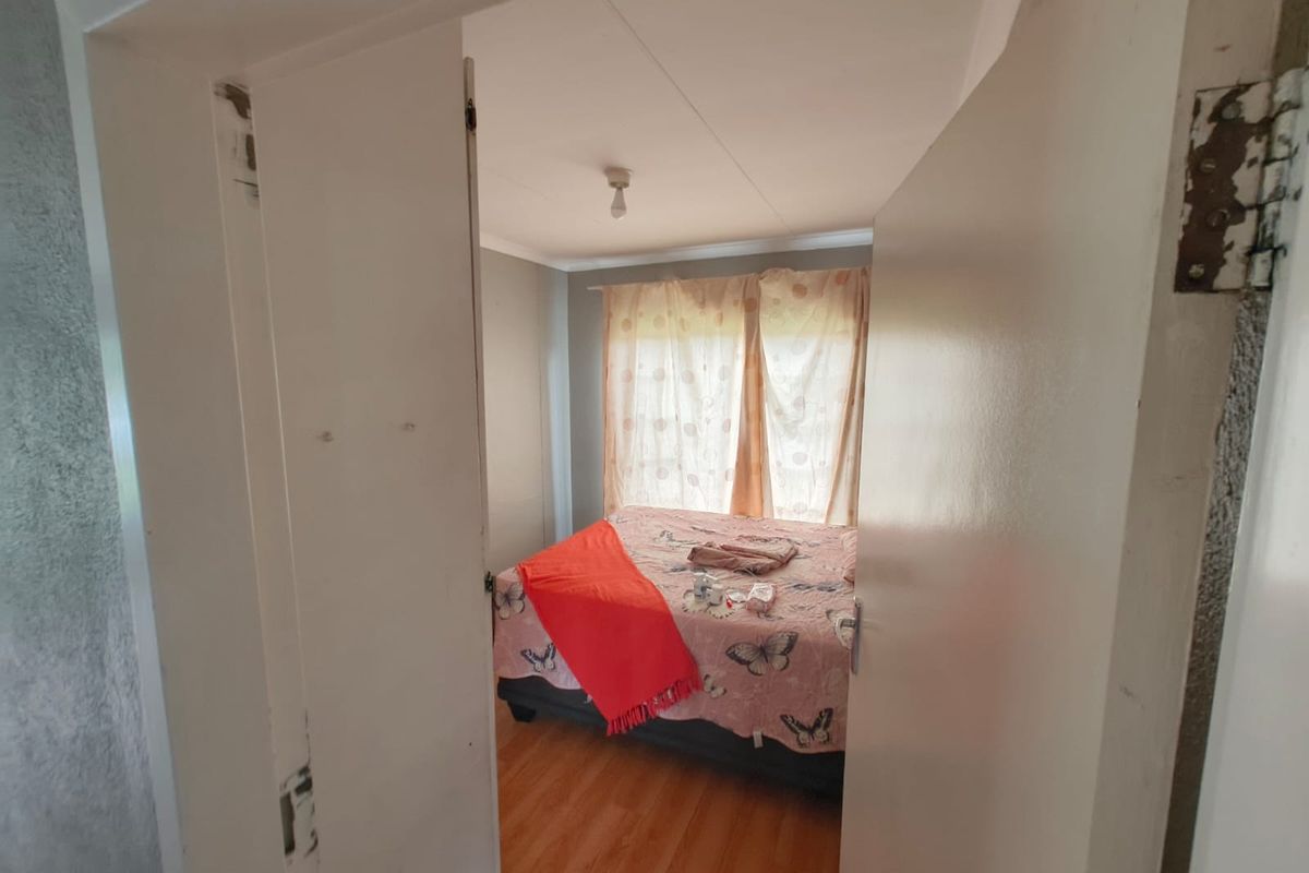A bedroom featuring laminate flooring and a neutral wall finish, viewed through a doorway with visible wear on the door frame and hinges.