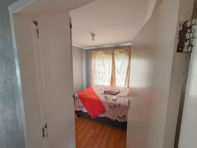 A bedroom featuring laminate flooring and a neutral wall finish, viewed through a doorway with visible wear on the door frame and hinges.