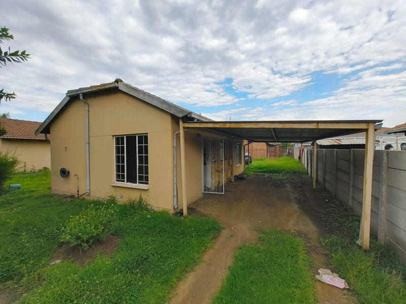 Exterior view of a detached house featuring a carport, precast boundary wall, and a large yard area requiring landscaping and maintenance.