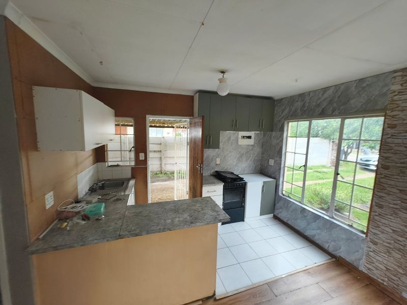 A functional kitchen space featuring built-in cabinetry, a freestanding stove, and direct access to the rear exterior, offering potential for modernization and cosmetic updates.