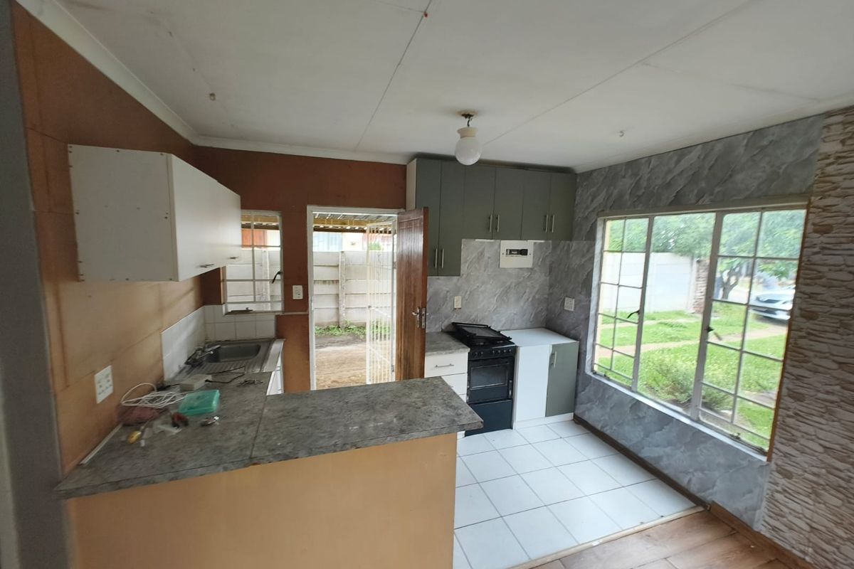A functional kitchen space featuring built-in cabinetry, a freestanding stove, and direct access to the rear exterior, offering potential for modernization and cosmetic updates.