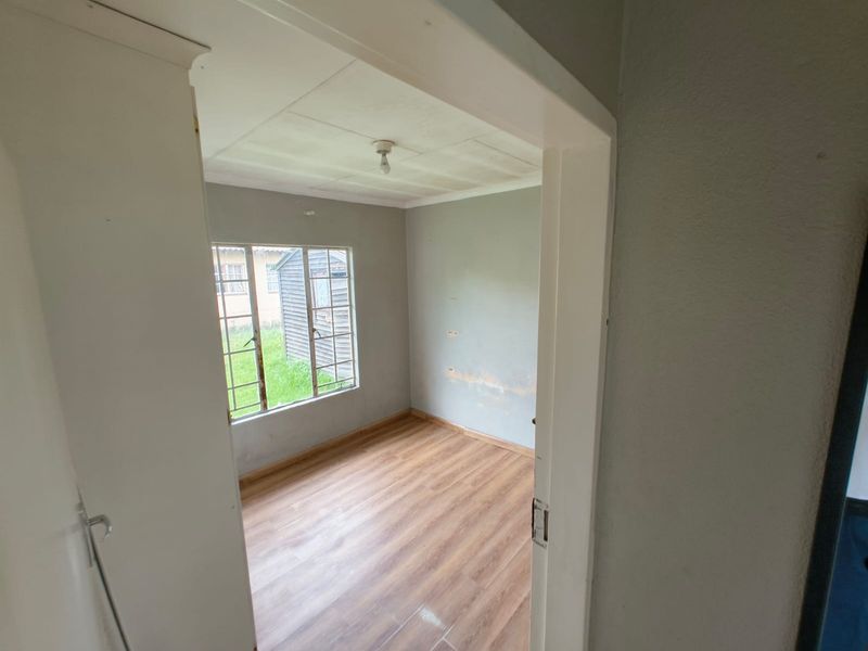 An empty bedroom featuring laminate flooring, steel-framed windows, and ceiling tiles, requiring minor wall repairs and cosmetic updates.