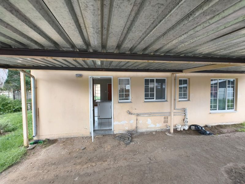 Rear exterior view of the property featuring a covered patio area with corrugated metal roofing, exposed brickwork, and visible exterior plumbing.