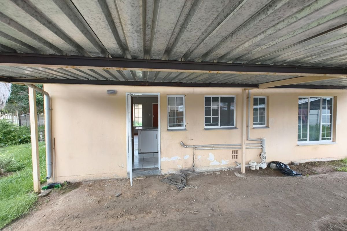 Rear exterior view of the property featuring a covered patio area with corrugated metal roofing, exposed brickwork, and visible exterior plumbing.