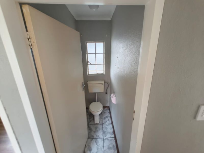 A compact, functional guest toilet featuring tiled flooring and a window, currently in need of cosmetic updates to improve its overall condition.