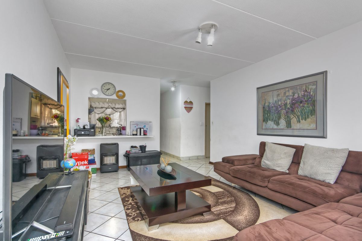 A living room featuring tiled flooring and a pass-through window connecting to the kitchen area, providing an open feel to the apartment layout.