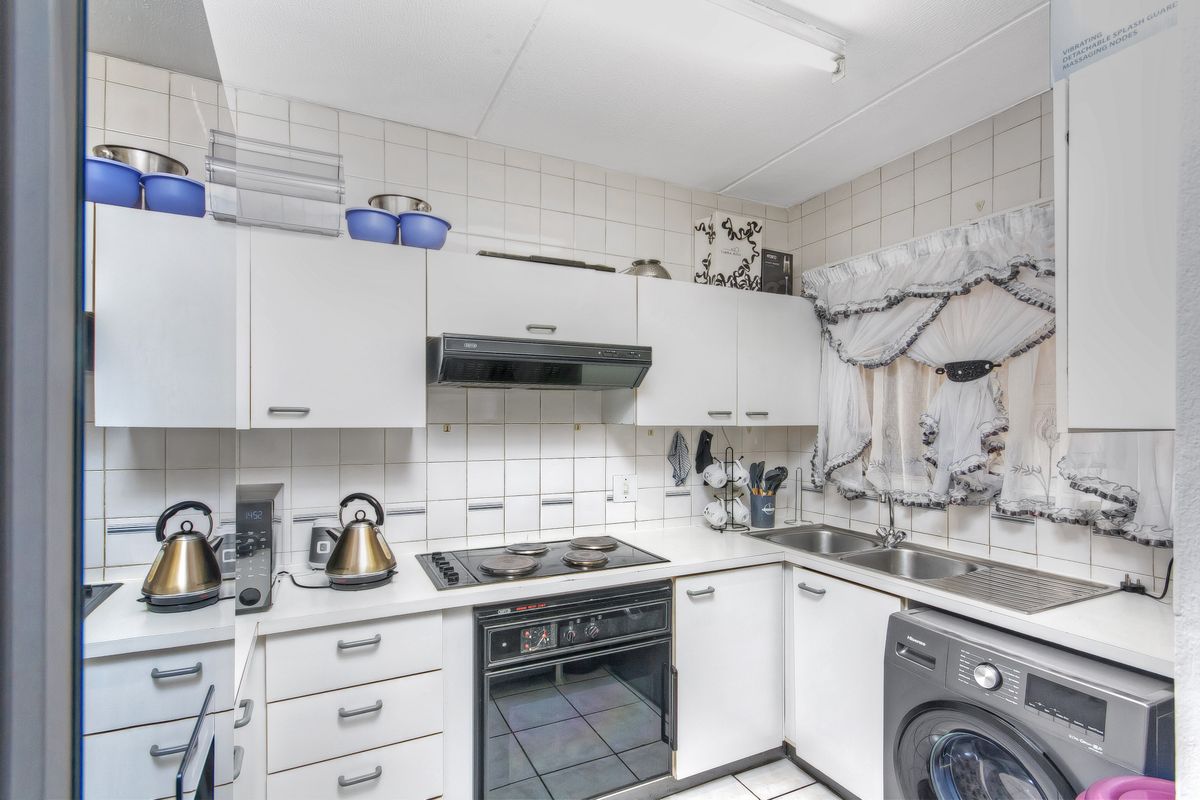 A functional kitchen featuring white cabinetry, an integrated electric hob and oven, extractor fan, and a double sink with tiled backsplash and flooring.