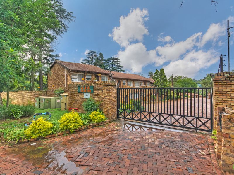 Front entrance view of the apartment complex featuring a secure metal gate, brick perimeter wall, and paved driveway access.