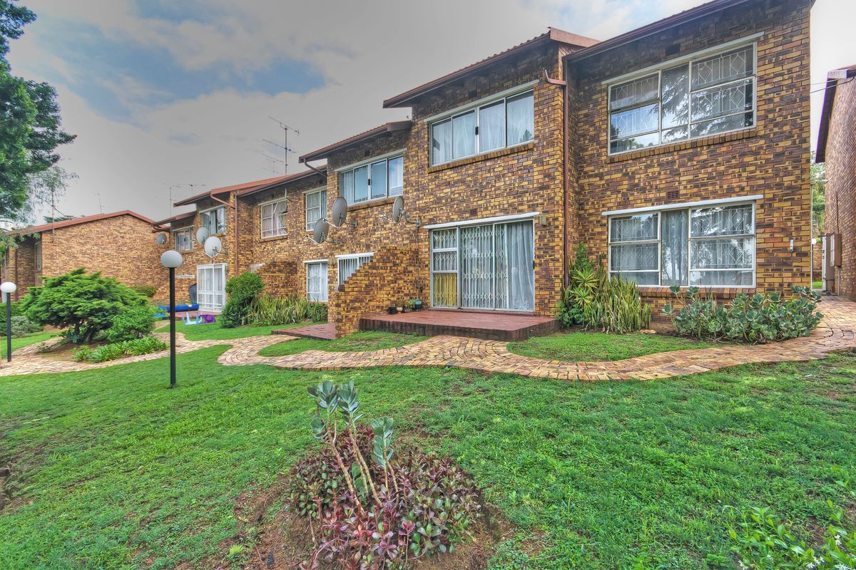 Rear view of a multi-story apartment complex featuring face brick construction, sliding glass doors, and a landscaped garden with paved walkways.