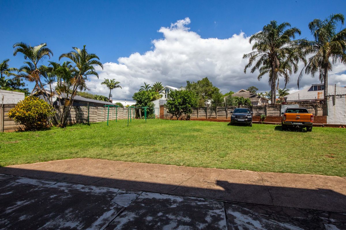 A spacious rear garden featuring a large lawn area, concrete patio, and perimeter boundary walling.