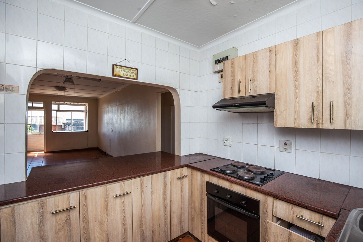 A functional kitchen featuring wood-look cabinetry, a built-in oven and hob, and a serving hatch opening into the adjacent living area.