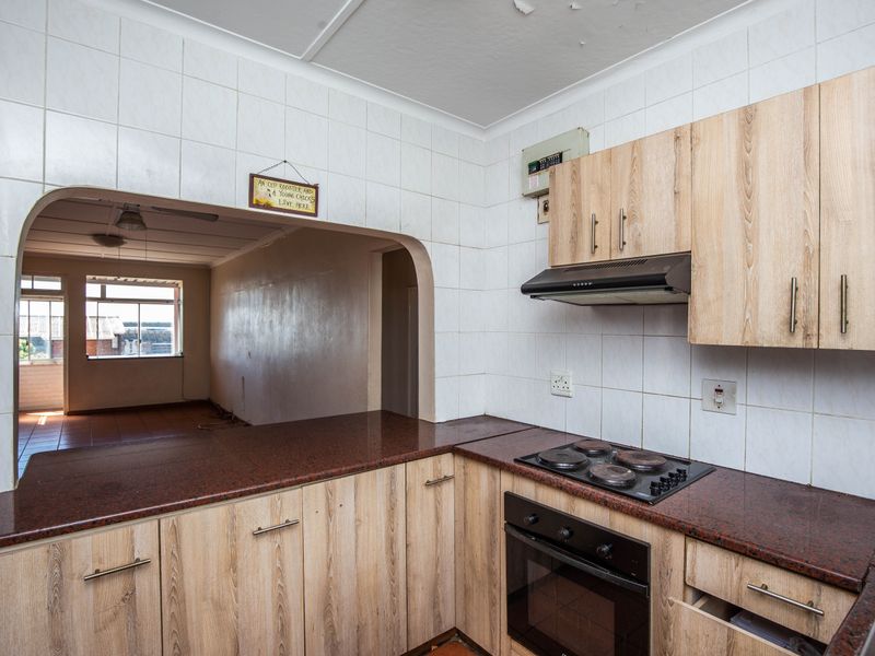 A functional kitchen featuring wood-look cabinetry, a built-in oven and hob, and a serving hatch opening into the adjacent living area.