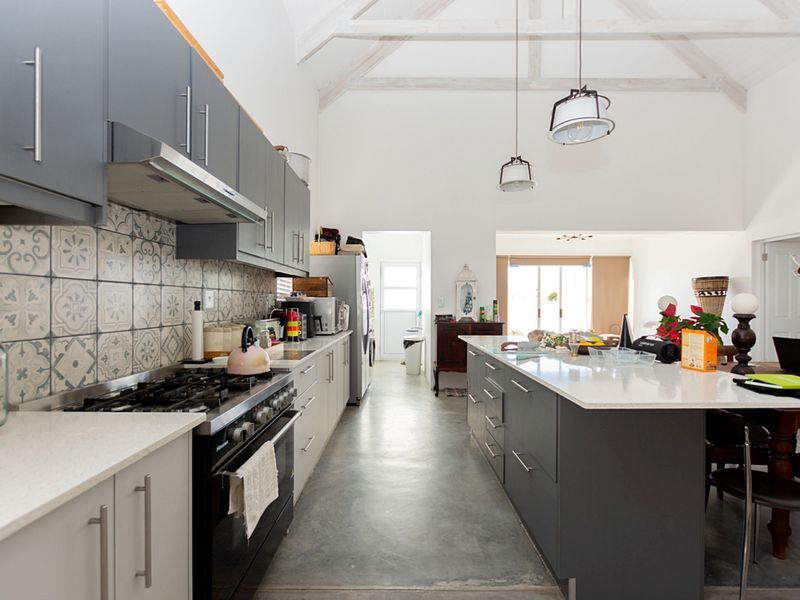 Spacious open-plan kitchen featuring a large island, gas stove, quartz countertops, patterned backsplash, and high vaulted ceilings with exposed timber trusses.