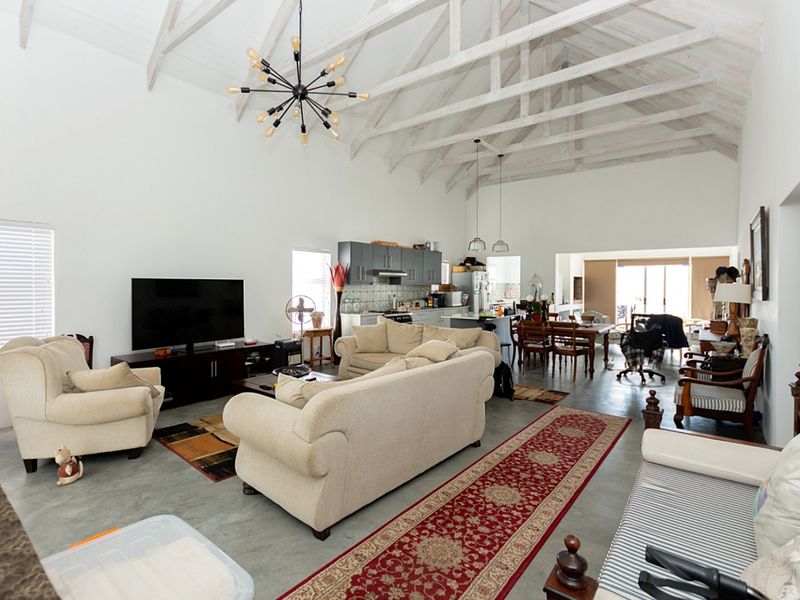 Spacious open-plan living area featuring high vaulted ceilings with exposed timber trusses, polished concrete floors, and a modern integrated kitchen.