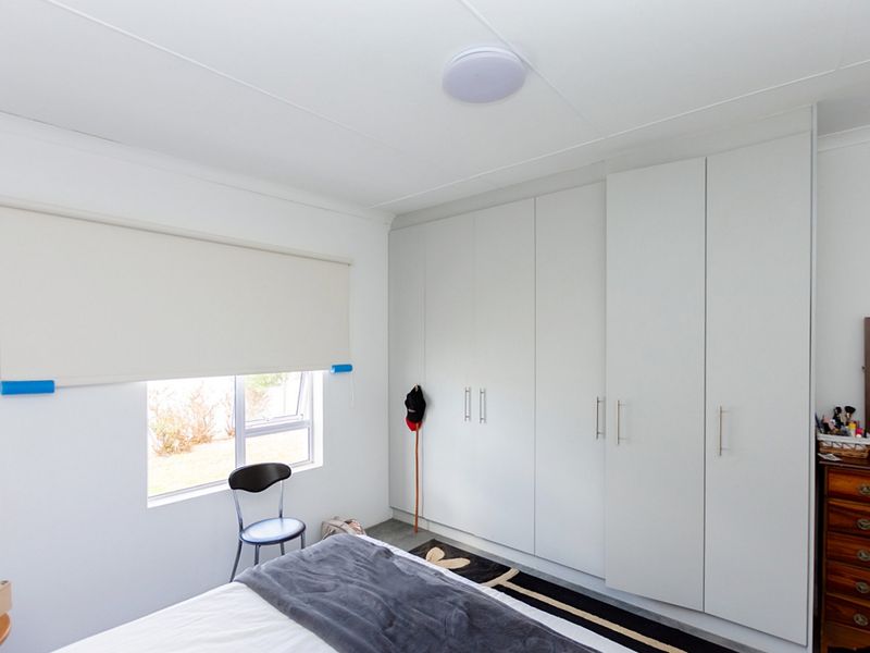 A bright bedroom featuring extensive floor-to-ceiling built-in cupboards, a neutral roller blind, and a clean, minimalist aesthetic.