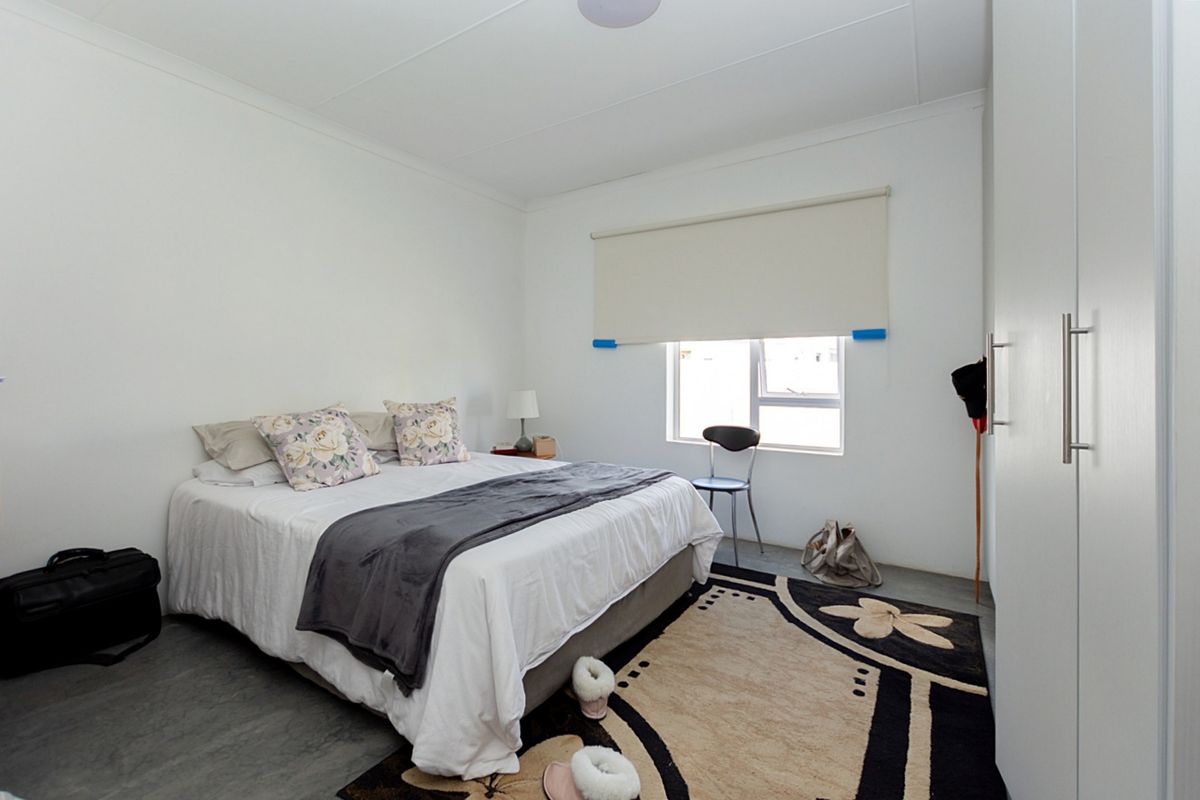 A functional bedroom featuring a built-in wardrobe, neutral walls, and a roller blind over a sliding window.