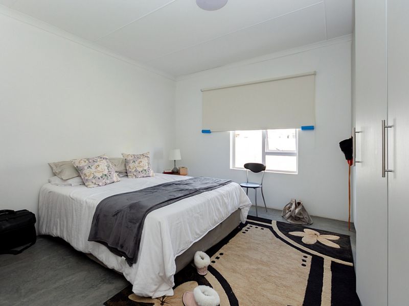 A functional bedroom featuring a built-in wardrobe, neutral walls, and a roller blind over a sliding window.