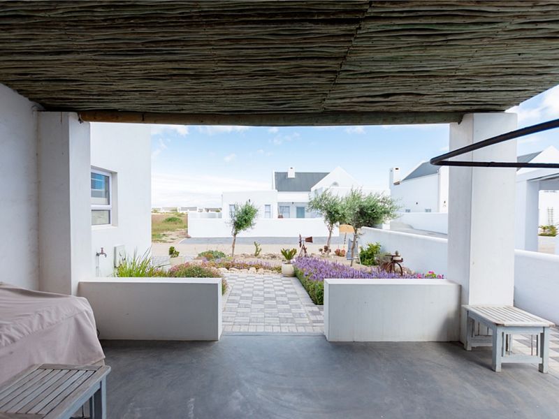 A covered patio featuring a rustic thatched roof and concrete flooring, overlooking a landscaped garden and paved pathway.