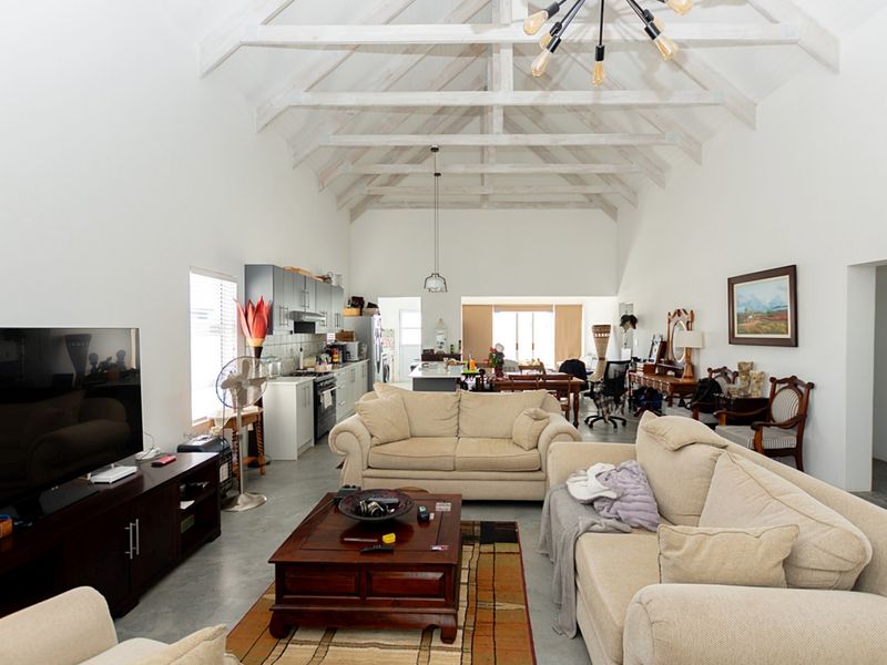 Spacious open-plan living area featuring a high vaulted ceiling with exposed timber trusses, polished concrete floors, and a modern integrated kitchen.