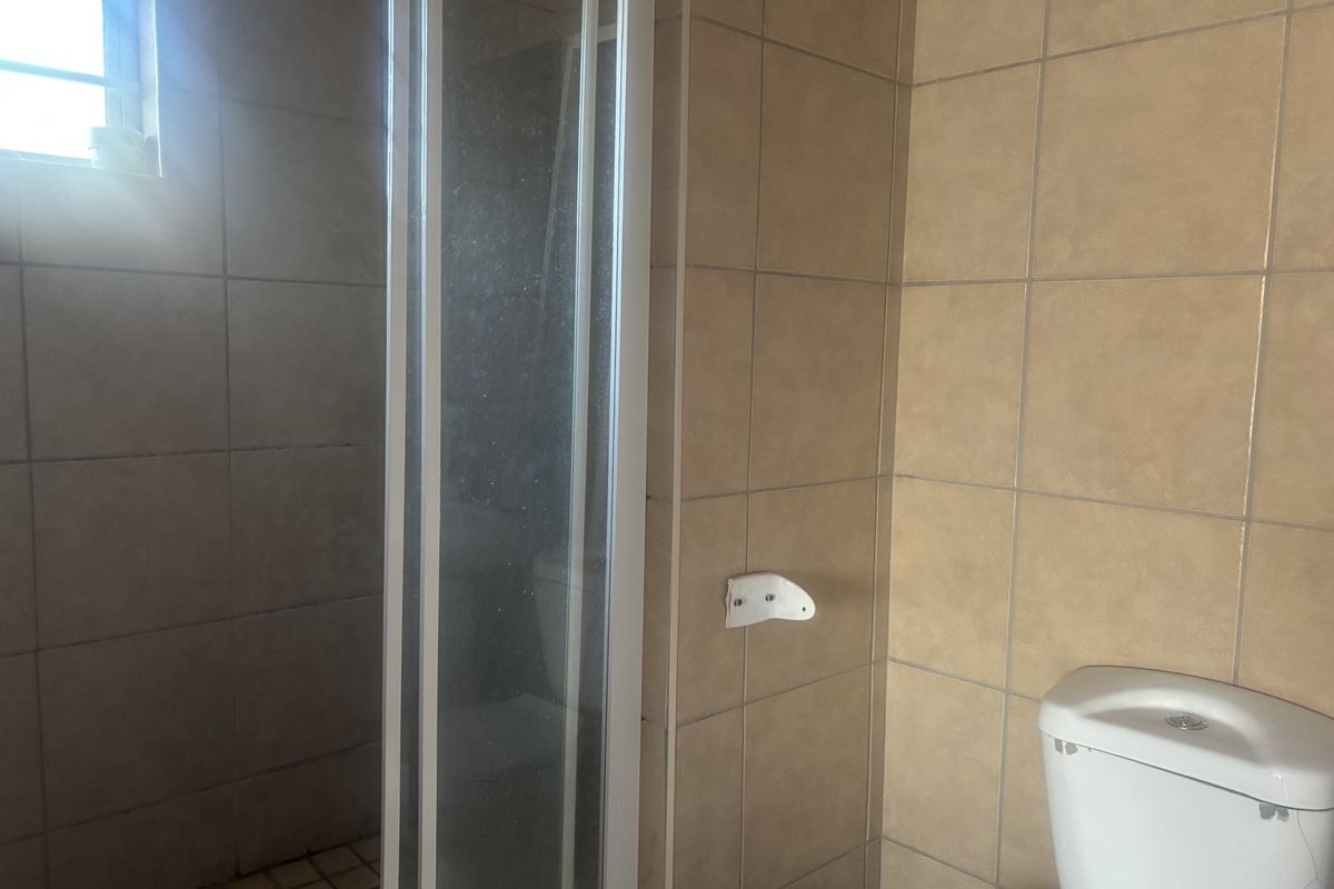 A functional bathroom featuring a shower enclosure with a glass door and a standard toilet, finished with neutral wall and floor tiling.