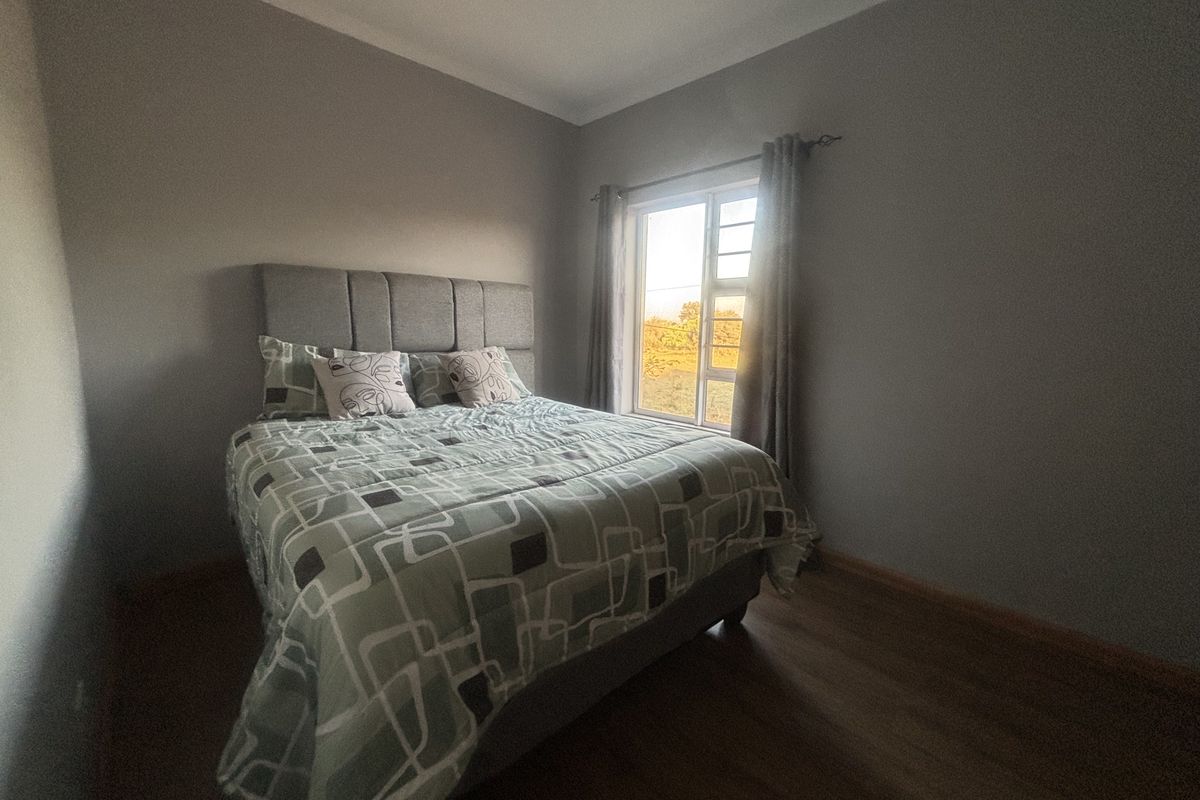 A bedroom featuring laminate flooring, neutral wall paint, and a window providing natural light.